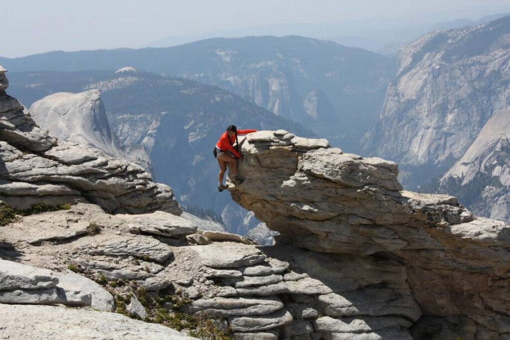 Half Dome appears in the background, left, while a hike strikes a daring pose atop Clouds Rest.